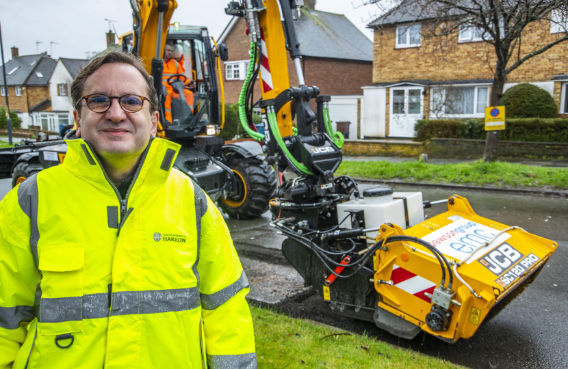 Cllr Paul Osborn desked in high-viz stood in front of the JCB pothole pro machine. In the background are residential houses.