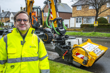 Cllr Paul Osborn desked in high-viz stood in front of the JCB pothole pro machine. In the background are residential houses.